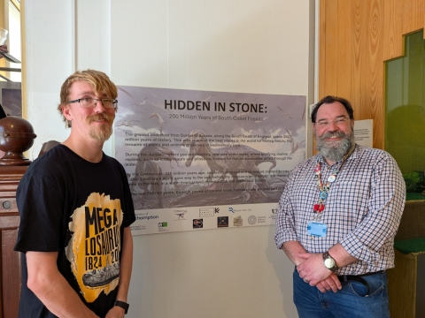 Two academics stood by a sign for the Hidden in Stone exhibition