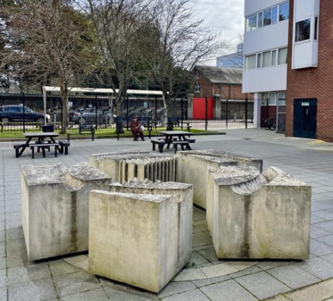 Photo of the concrete 'Squareinthecircle' sculpture outside of the Lion Gate university building with trees and bikes in the background