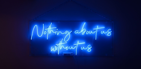 Nothing About Us Without Us in blue neon lights