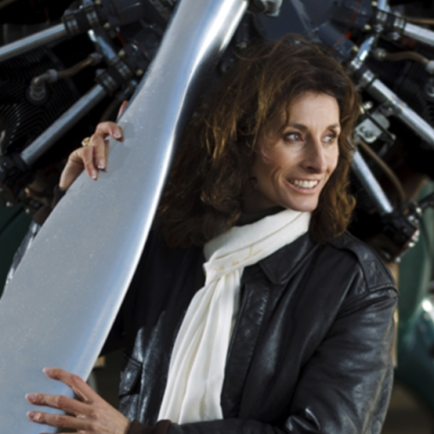 Tracey Curtis Taylor in leather jacket and scarf leaning against plane