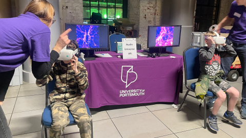 Two people using VR headsets, while sat next to a University of Portsmouth stall at the Stargazing at the Historic Dockyard event