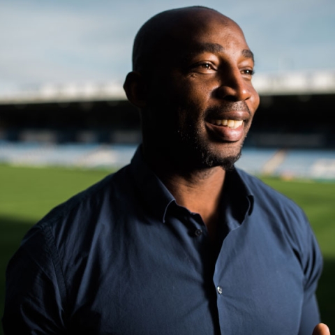Alumnus Vincent Pericard on Portsmouth Football Club pitch smiling to camera in blue shirt