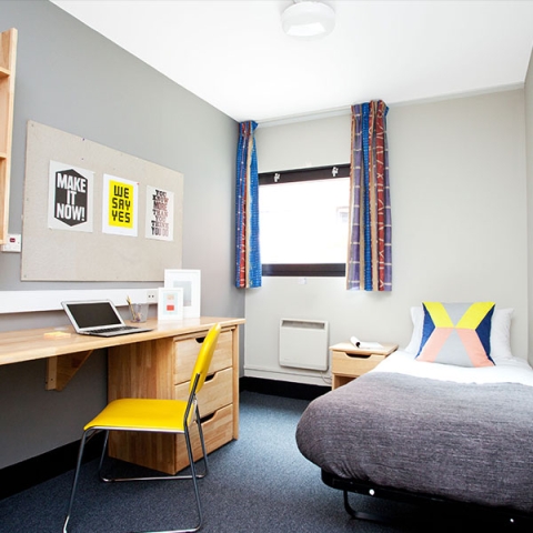 A bedroom in student halls with bed, desk, and chair