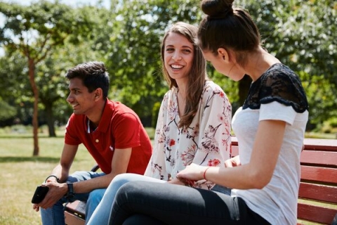 Three students smiling and sitting outside on red bench