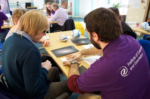 A photo from the Tactile Universe community event in January 2017 showing four people sitting around a table. The person in the front is explaining a tactile galaxy to the person on the left.