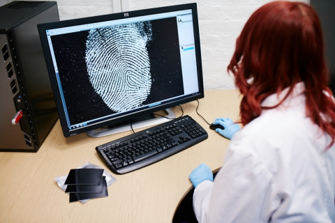 Female forensics working studying fingerprint on computer