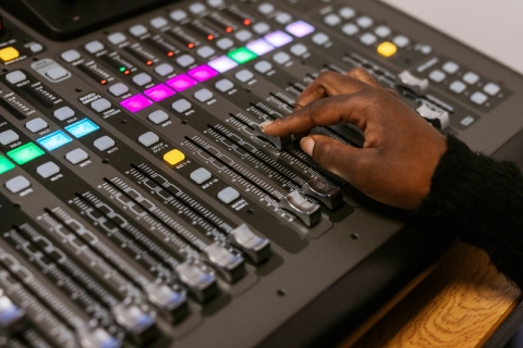 Close up of an audio mixer with a person's hand on a slider