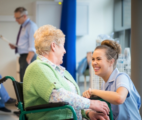 Female nurse speaking to elderly female patient in wheelchair