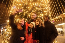 Students in winter clothes taking a pictures in front of a lit up Christmas tree
