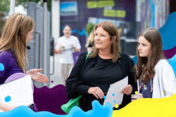 A woman and a girl listen to a female ambassador holding a prospectus 