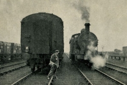 Black and white picture of a man crossing train tracks in front of two trains.