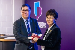 Chris Chang and honoured guest exchanging a gift wrapped with white paper and a red ribbon.
