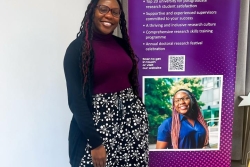 International Student Ritah smiling next to a promotional banner with her photo on