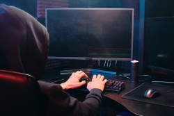 Person with a black hood up typing on a computer