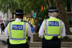 Two police officers with their backs to camera, showing their high visibility vests that say 'police'