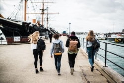 Four students walk along waterside at Portsmouth's Historic Dockyard