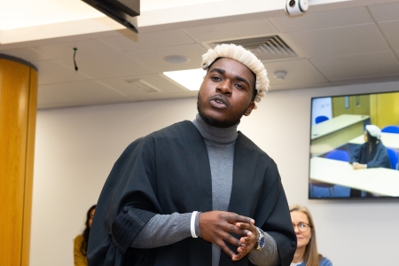A man standing in a replica law court wearing a solicitors robe a white periwig