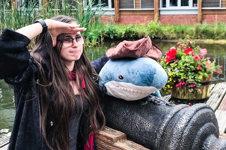 Sarah saluting to her left near a plush whale atop a mini-cannon