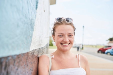 Female student in glasses and white top leaning against the wall in summer
