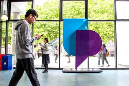 Person walking past a University of Portsmouth logo in the Dennis Sciama foyer