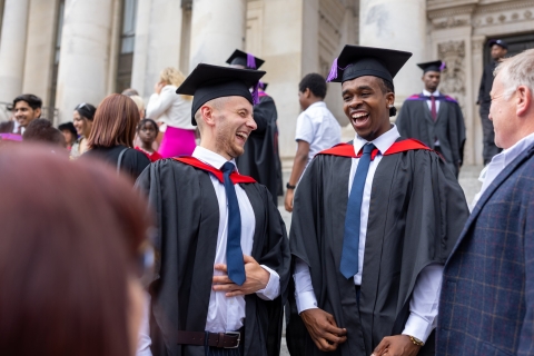 Two students laughing together on graduation day outside Portsmouth Guildhall