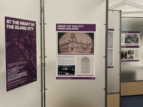 A picture of the exhibition 'At the Heart of the Island City' with four poster boards shown, one of which is the title board and the other is titled 'Heart of the City: Park Building' with a picture of Park Building