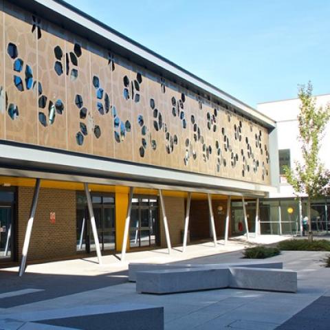 A modern building with decorative cladding and paved courtyard with seating, part of Eastleigh College