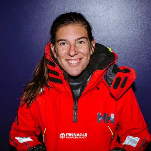 Ella wearing a red sailing coat smiling in front of a purple wall